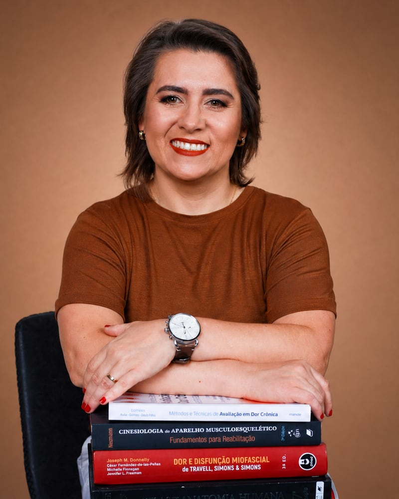 Vanessa Minotto, fisioterapeuta da Nauta, apoiada em uma pilha de livros de fisioterapia